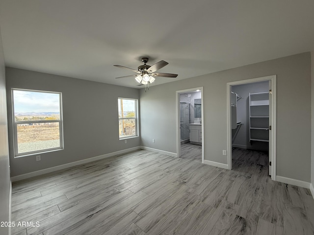 unfurnished bedroom featuring ceiling fan, ensuite bathroom, light hardwood / wood-style floors, a spacious closet, and a closet