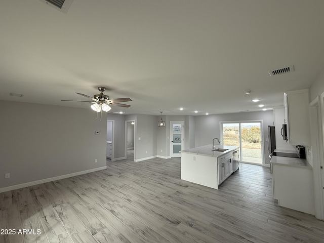 kitchen featuring white cabinetry, an island with sink, sink, ceiling fan, and light wood-type flooring