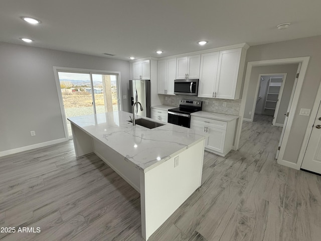 kitchen with sink, a center island with sink, appliances with stainless steel finishes, light stone countertops, and white cabinets