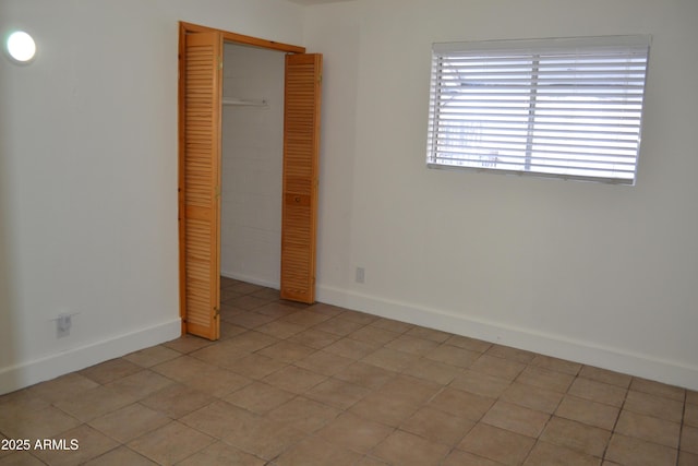 unfurnished bedroom with light tile patterned flooring, baseboards, and a closet