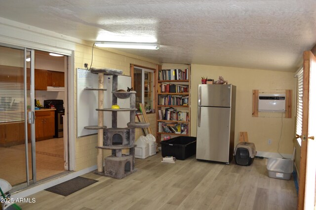 miscellaneous room featuring a wall mounted AC, concrete block wall, light wood finished floors, and a textured ceiling