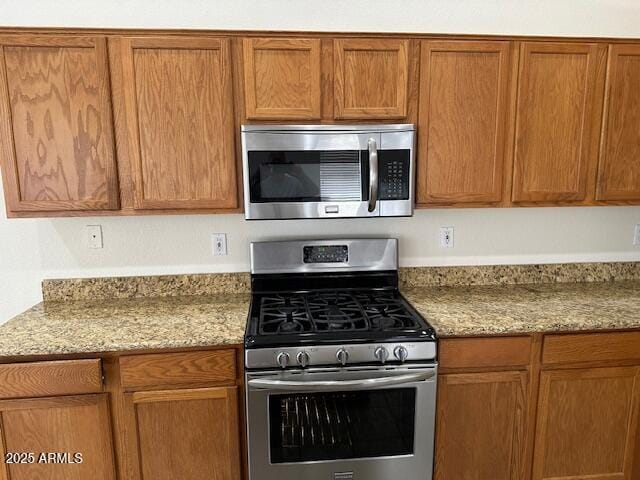 21192 N 80th Ln, Peoria, AZ 85382 - kitchen with stainless steel appliances, light stone countertops, and brown cabinets