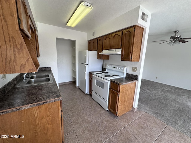 kitchen with white appliances, dark countertops, carpet floors, under cabinet range hood, and a sink