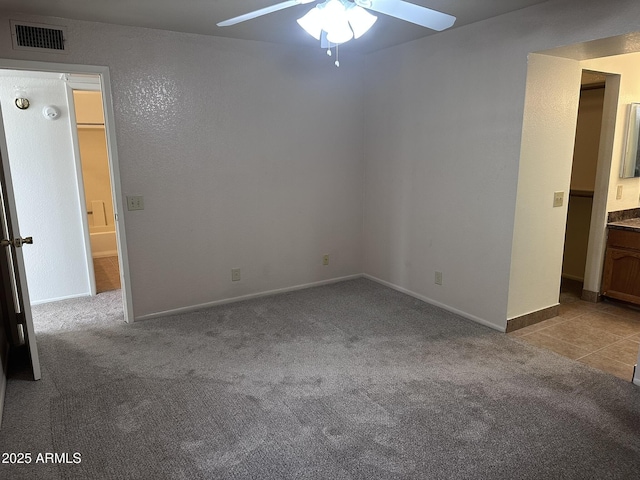 unfurnished bedroom featuring carpet floors, visible vents, connected bathroom, baseboards, and tile patterned floors