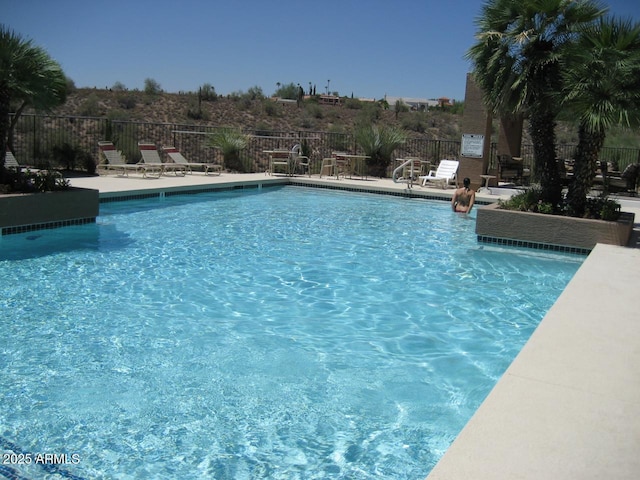 community pool with a patio area and fence