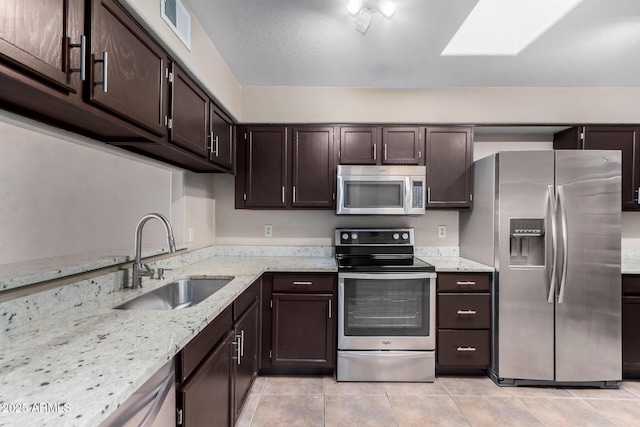 kitchen with dark brown cabinetry, visible vents, appliances with stainless steel finishes, light stone counters, and a sink