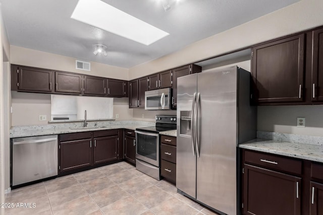 kitchen with dark brown cabinetry, a skylight, visible vents, stainless steel appliances, and a sink