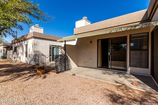 property entrance featuring a patio area, fence, a chimney, and stucco siding