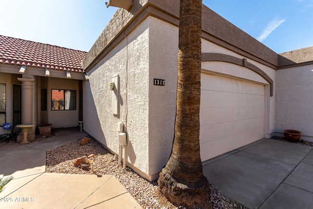 view of home's exterior featuring concrete driveway, a tiled roof, an attached garage, and stucco siding