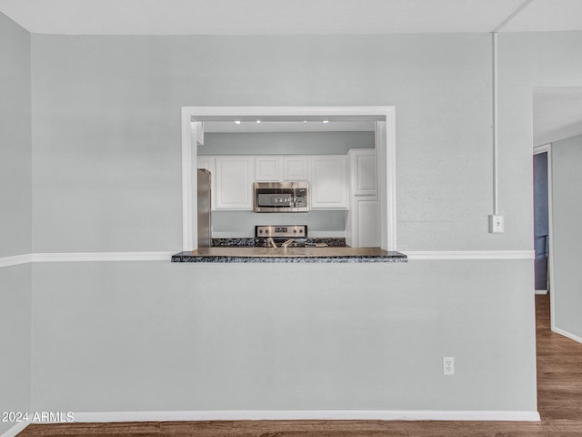 kitchen with dark countertops, appliances with stainless steel finishes, white cabinets, and wood finished floors