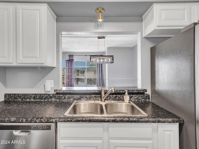kitchen with white cabinets, dark countertops, a notable chandelier, appliances with stainless steel finishes, and a sink
