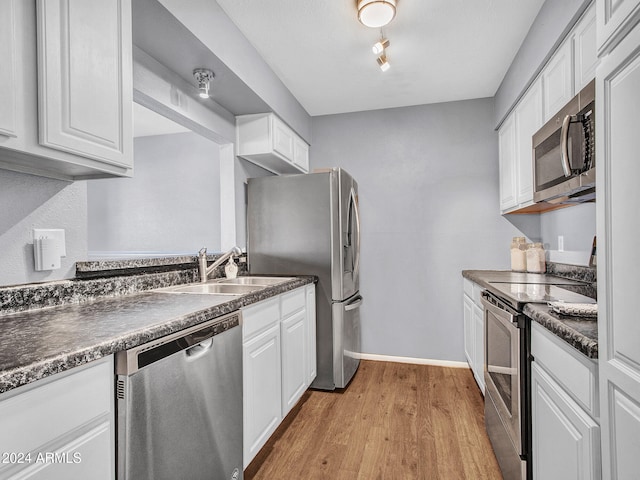kitchen with dark countertops, a sink, baseboards, white cabinets, and stainless steel appliances