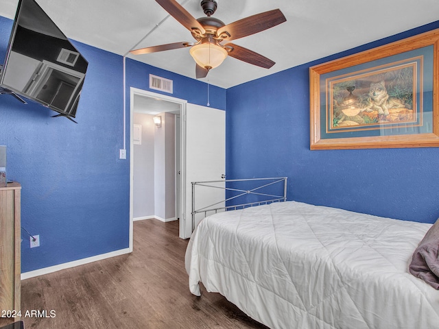 bedroom with visible vents, a textured wall, wood finished floors, baseboards, and ceiling fan