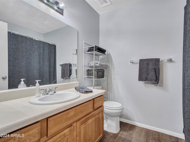 bathroom with vanity, toilet, baseboards, wood finished floors, and visible vents