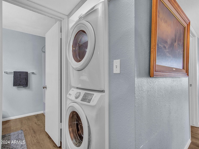 clothes washing area with laundry area, a textured wall, baseboards, wood finished floors, and stacked washer and clothes dryer