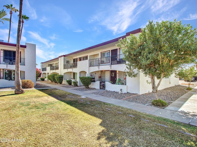 view of front facade featuring a front lawn, stucco siding, and a balcony