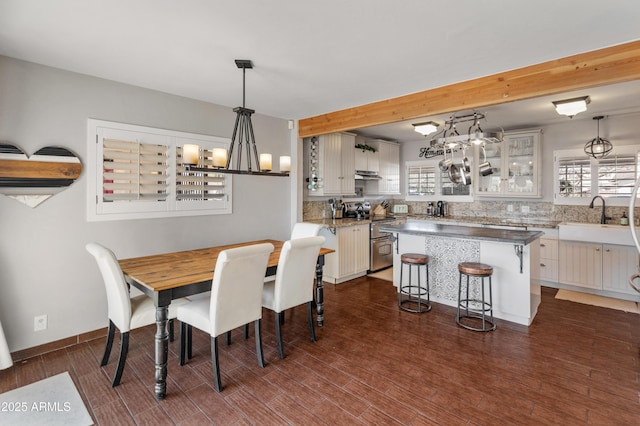 dining area featuring beamed ceiling, a wealth of natural light, dark hardwood / wood-style flooring, and sink