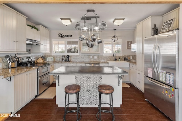 kitchen with white cabinets, appliances with stainless steel finishes, a center island, decorative light fixtures, and a kitchen breakfast bar