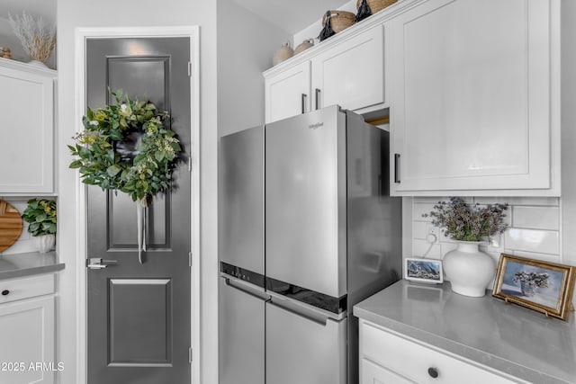 kitchen featuring white cabinets, freestanding refrigerator, and tasteful backsplash