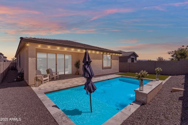 pool at dusk featuring a fenced in pool, a fenced backyard, and a patio area