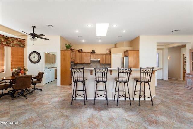 kitchen featuring ceiling fan, tasteful backsplash, a breakfast bar area, a skylight, and stainless steel fridge