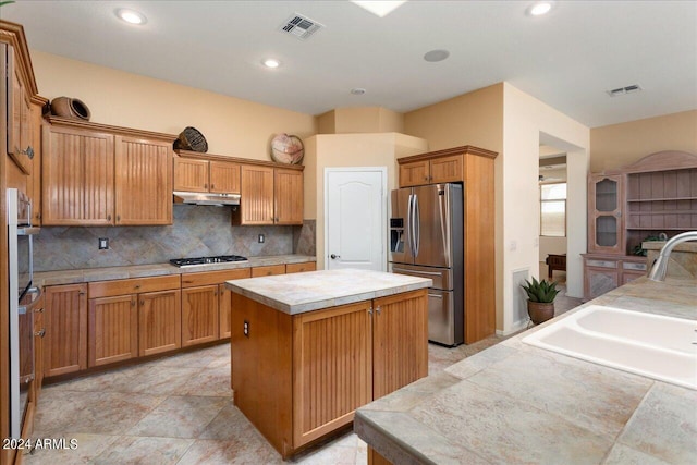 kitchen featuring appliances with stainless steel finishes, a center island, tile countertops, decorative backsplash, and sink