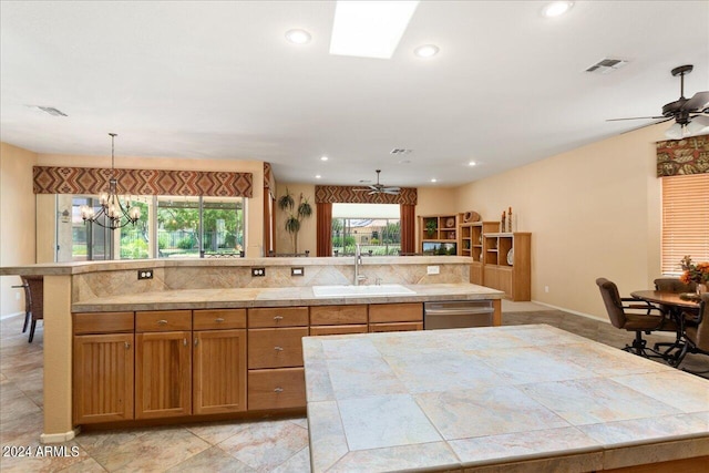 kitchen with a large island, tasteful backsplash, dishwasher, sink, and ceiling fan with notable chandelier