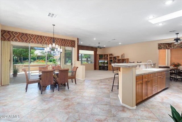 interior space featuring sink, decorative light fixtures, a kitchen breakfast bar, ceiling fan with notable chandelier, and a center island with sink