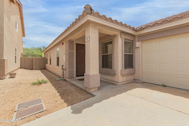 view of side of property with stucco siding, fence, a garage, driveway, and a tiled roof