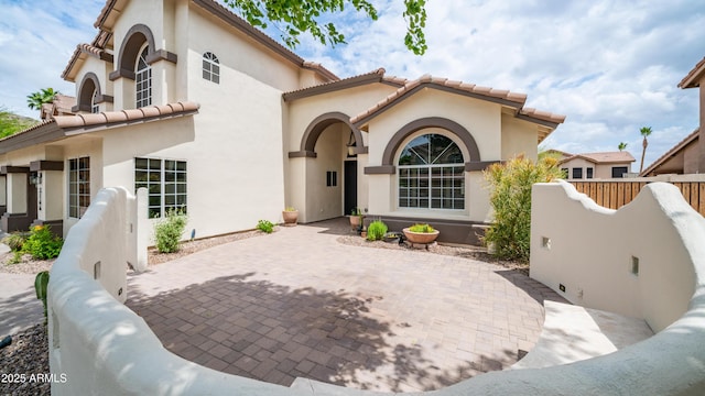 back of house with stucco siding, a tiled roof, a patio, driveway, and fence