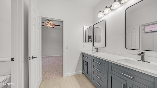 full bath with toilet, double vanity, a ceiling fan, and baseboards