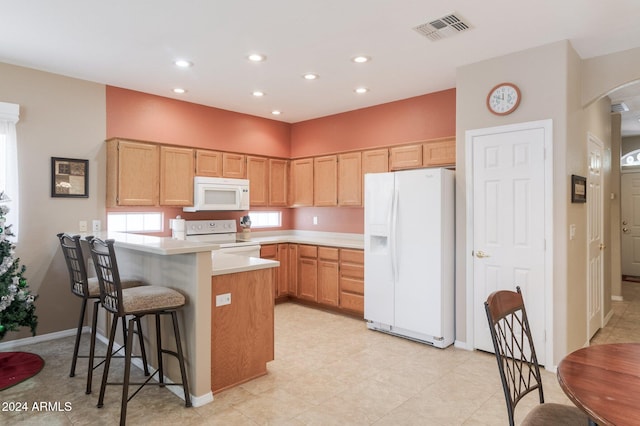 kitchen with a breakfast bar, light brown cabinets, and white appliances