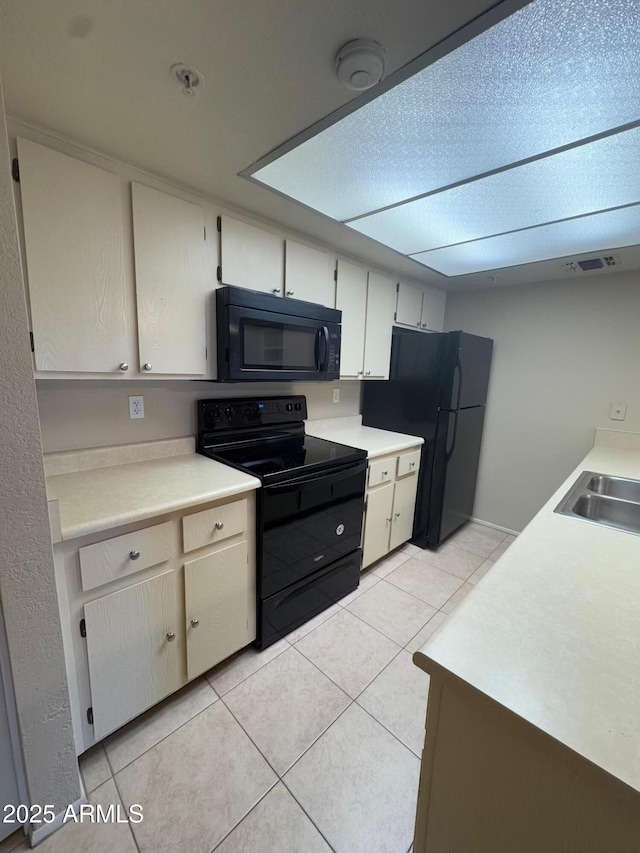 kitchen with white cabinetry, sink, light tile patterned floors, and black appliances