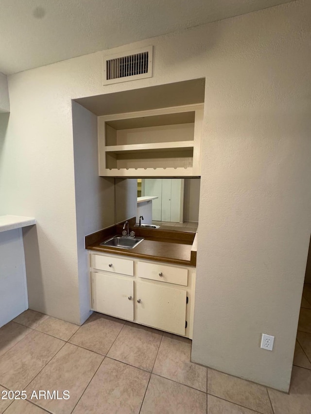 kitchen featuring sink, light tile patterned floors, and white cabinets