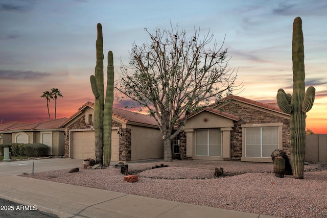 view of front of home featuring driveway, stucco siding, stone siding, a garage, and a tiled roof