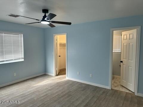 unfurnished bedroom featuring ceiling fan, ensuite bathroom, a spacious closet, and light hardwood / wood-style flooring