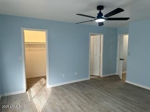 unfurnished bedroom featuring ceiling fan, a spacious closet, hardwood / wood-style floors, and a closet