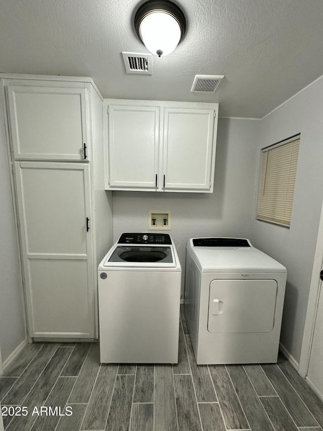 laundry area with cabinets, a textured ceiling, and independent washer and dryer