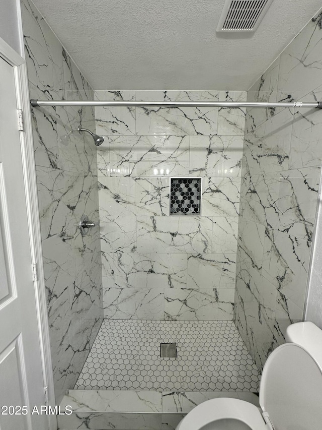 bathroom featuring toilet, a textured ceiling, and a tile shower