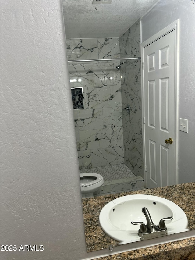 bathroom featuring a textured ceiling, toilet, and tiled shower