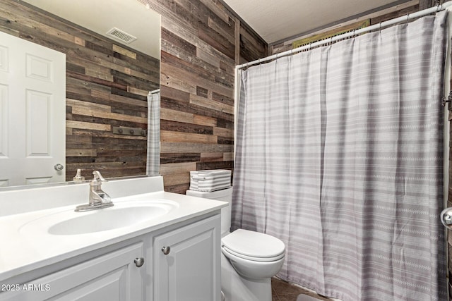 full bath with toilet, vanity, wooden walls, and visible vents