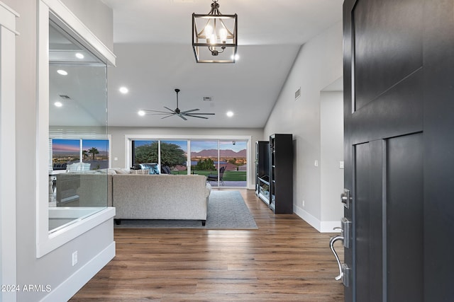 living room featuring ceiling fan with notable chandelier, dark wood-type flooring, and vaulted ceiling