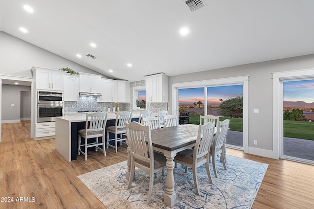 dining space featuring sink, vaulted ceiling, and light hardwood / wood-style floors