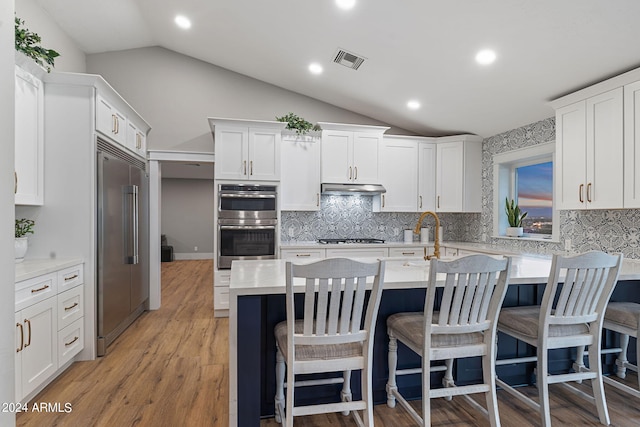 kitchen featuring stainless steel appliances, white cabinets, a breakfast bar, light hardwood / wood-style floors, and vaulted ceiling