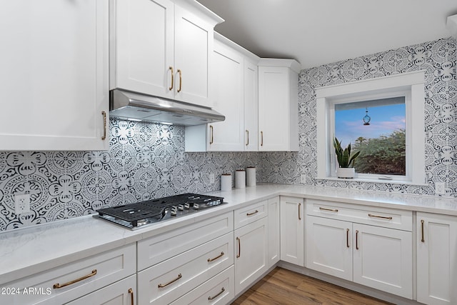 kitchen featuring decorative backsplash, light hardwood / wood-style floors, stainless steel gas stovetop, and white cabinetry