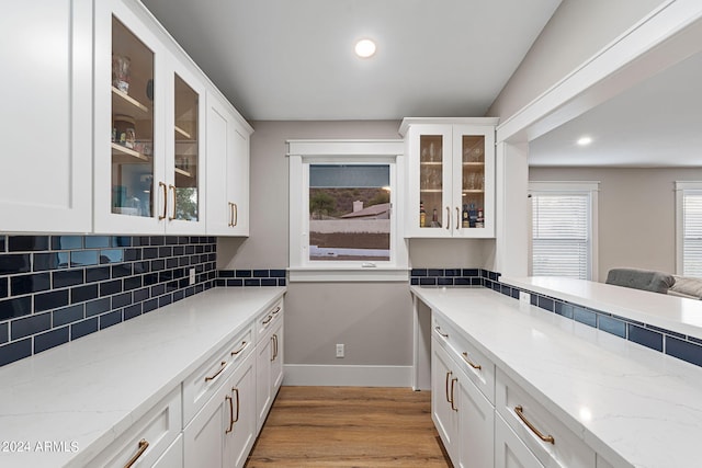 kitchen featuring tasteful backsplash, light stone counters, light hardwood / wood-style floors, and white cabinets