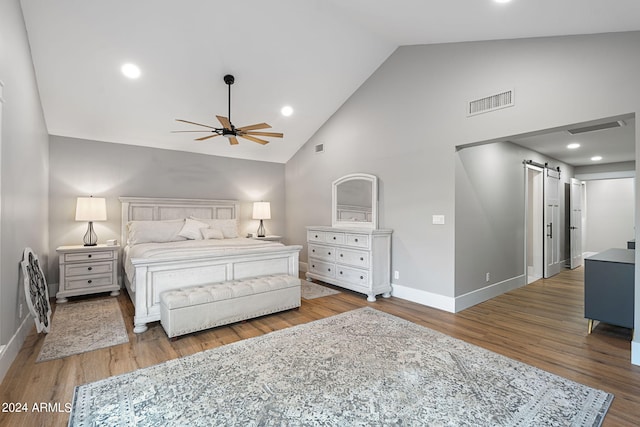 bedroom featuring a barn door, high vaulted ceiling, hardwood / wood-style flooring, and ceiling fan