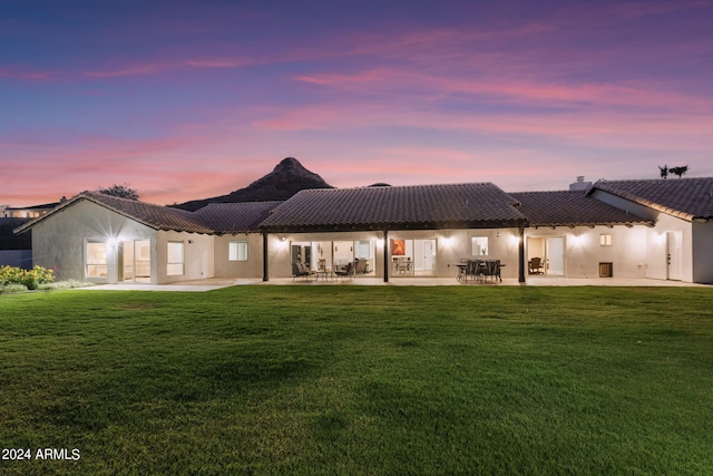 back house at dusk featuring a patio and a lawn