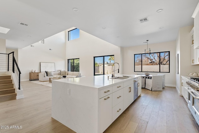 kitchen with sink, dishwasher, white cabinets, a center island with sink, and light wood-type flooring