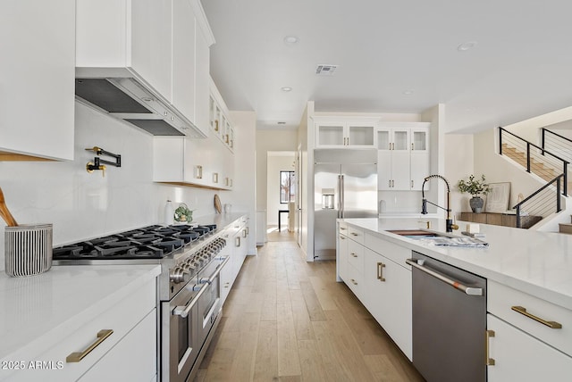 kitchen featuring sink, light hardwood / wood-style flooring, light stone counters, premium appliances, and white cabinets